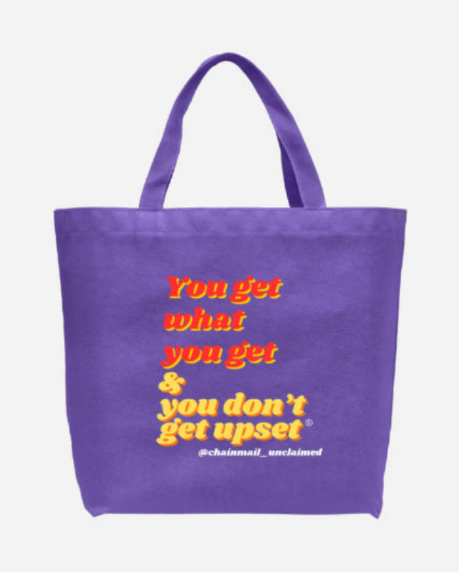 A purple canvas tote bag with yellow and orange text that reads 'You get what you get & you don't get upset' with the handle '@chainmail_ucclaimed' printed below it, shown against a plain light gray background.
